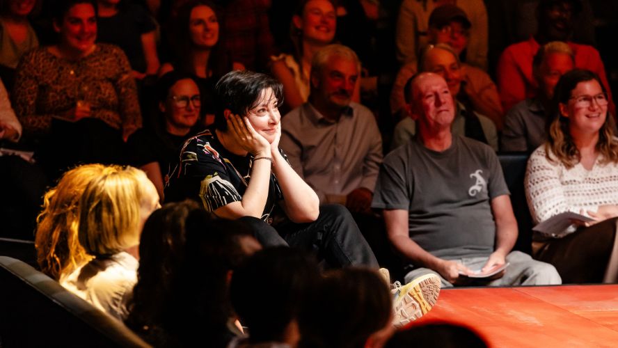 Sue Perkins sits on stage @sohoplace near the audience with her hands places on either side of her face.
